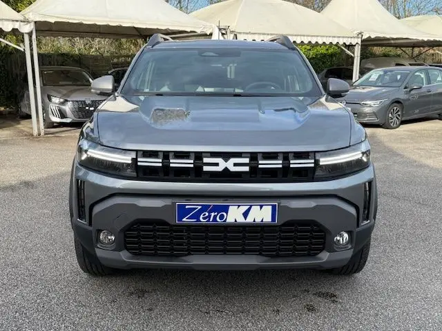 Vue frontale d'un Dacia Duster 1.8 Hybrid 155 Journey gris schiste avec calandre noire et plaques Zero KM.