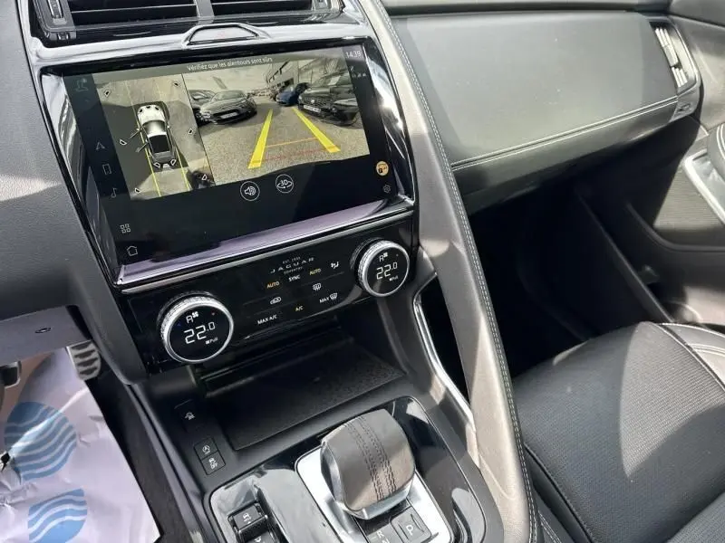 Vue intérieure centrée sur la console centrale du Jaguar E-PACE noir, avec écran tactile et commandes de climatisation visibles.