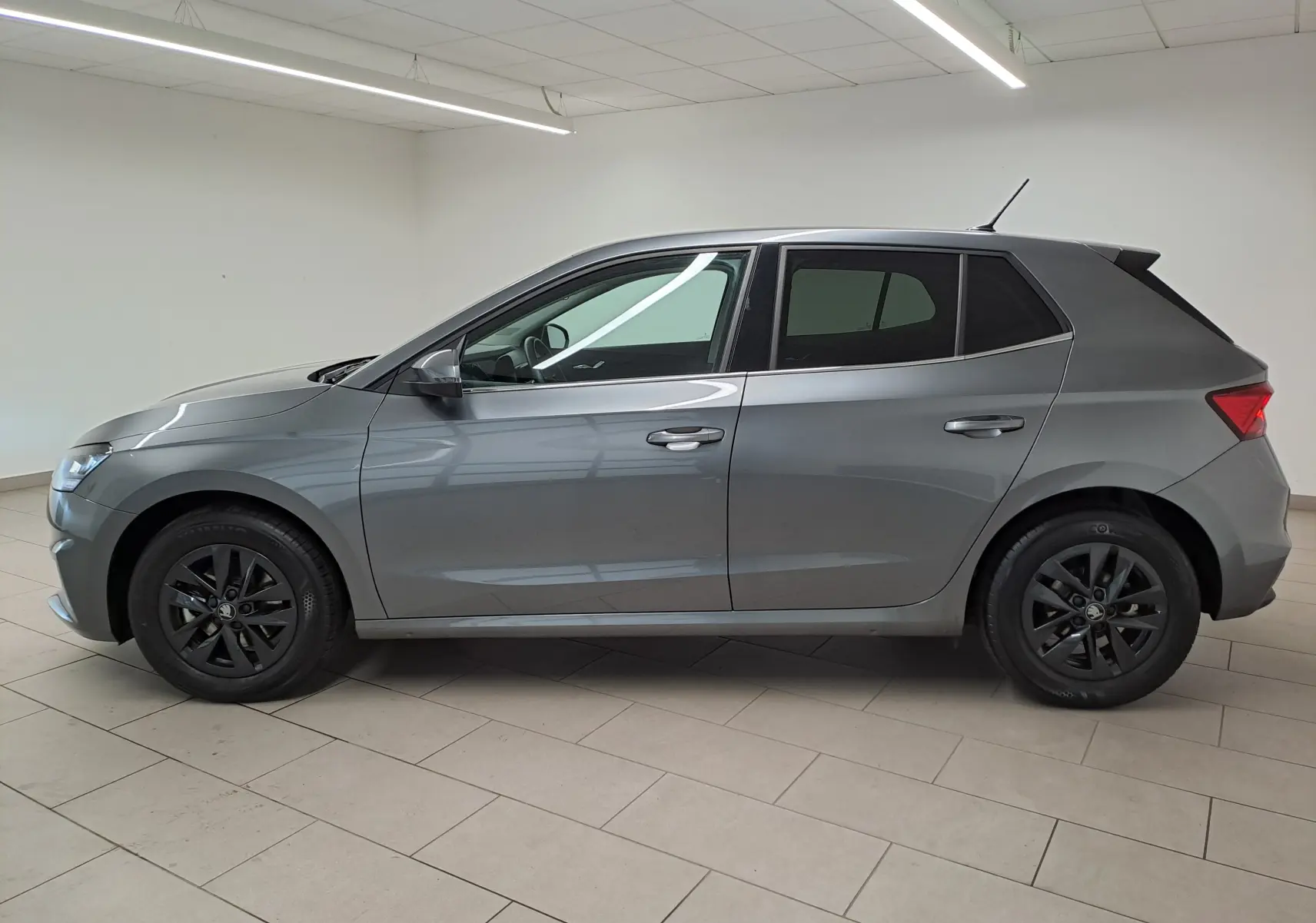 Profil côté gauche d'une Skoda Fabia 2025 gris graphite avec jantes alliage noires et vitres surteintées en intérieur blanc.