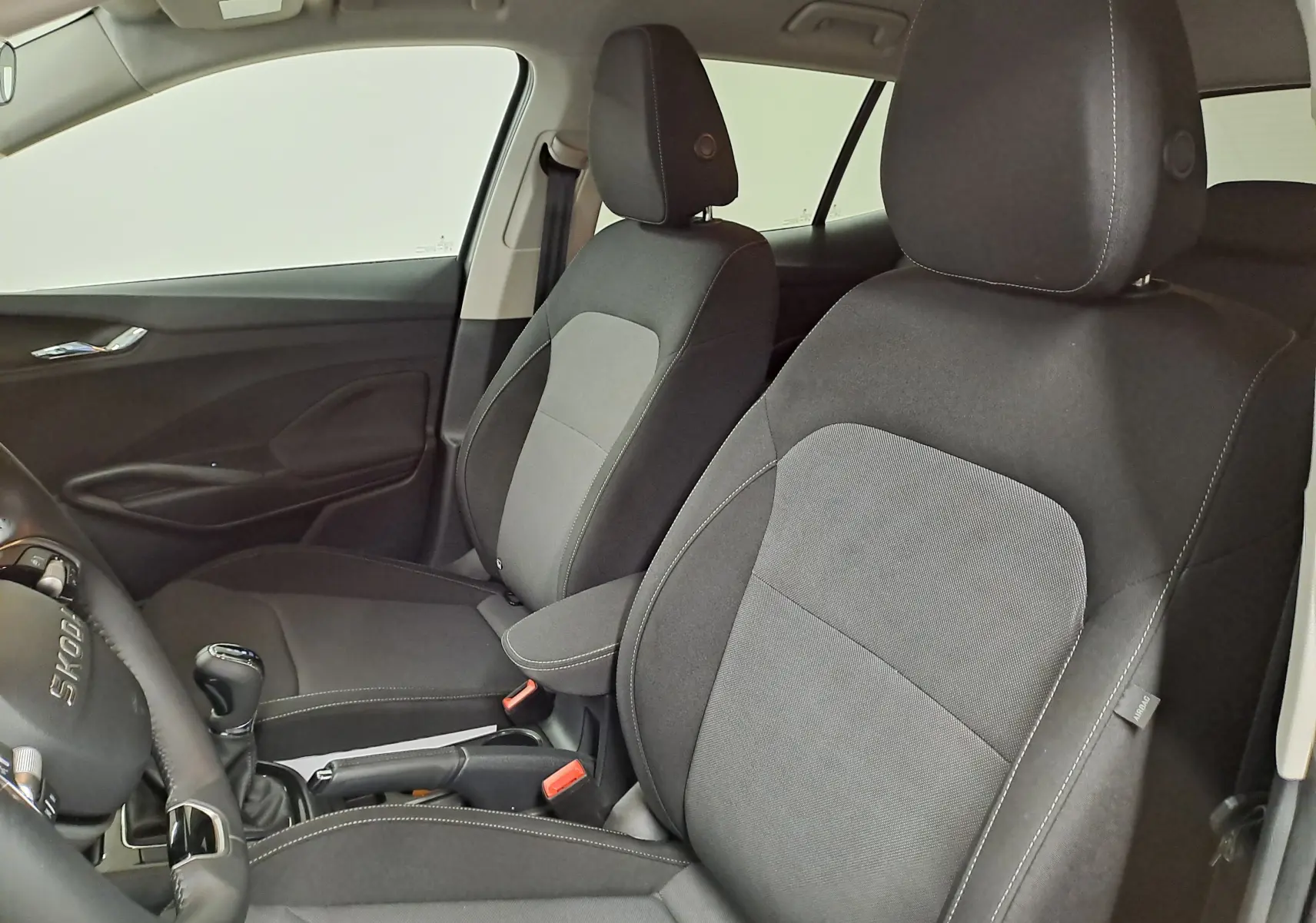 Vue intérieure côté conducteur et passager avant de la Skoda Fabia 2025 avec sièges tissu gris et volant cuir.