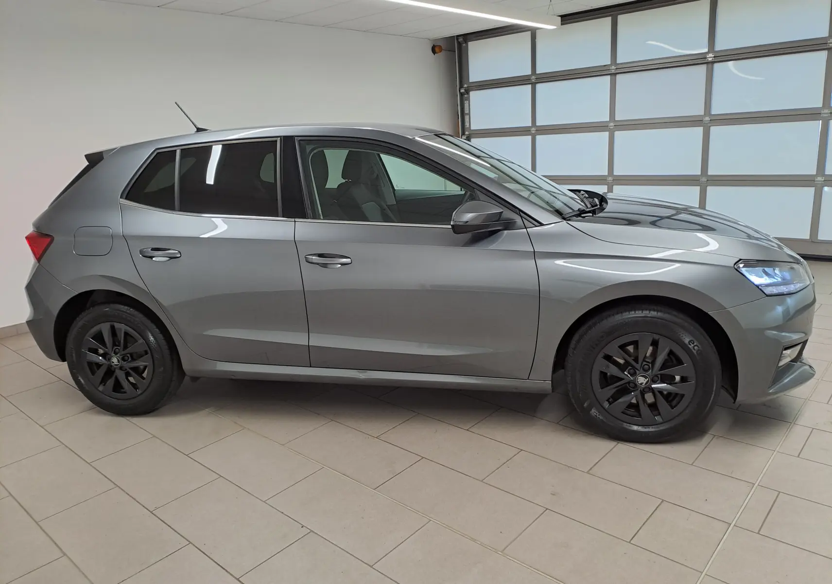 Vue de profil côté gauche d'une Skoda Fabia 2025 gris graphite avec jantes alliage noires et vitres surteintées.