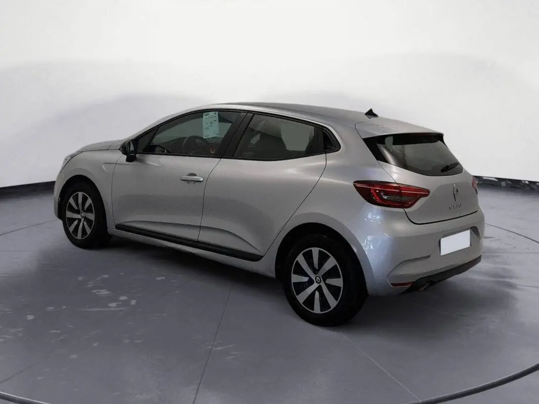 Vue 3/4 arrière côté gauche d'une Renault Clio gris clair 2022 avec jantes noires et vitres teintées.