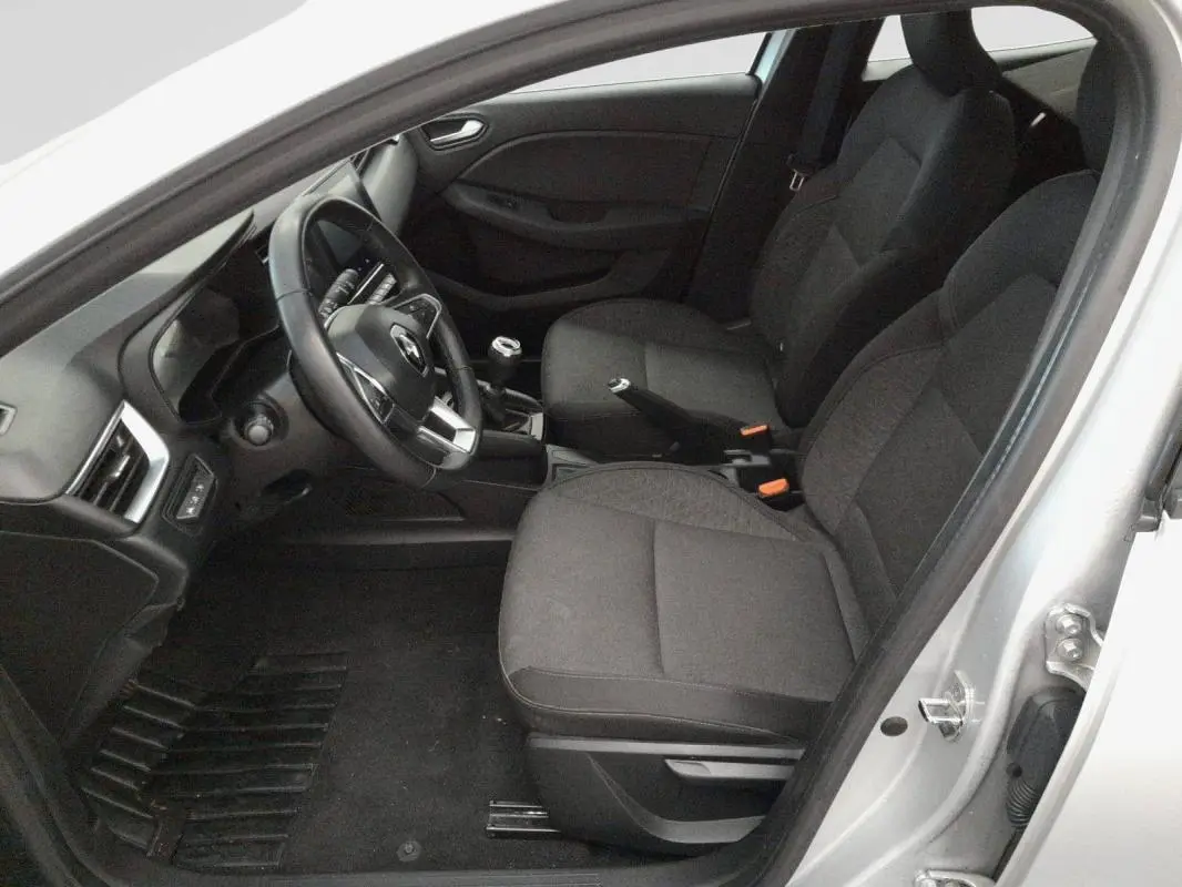Vue intérieure côté conducteur d'une Renault Clio gris clair 2022, sièges tissu noirs et volant multifonction.