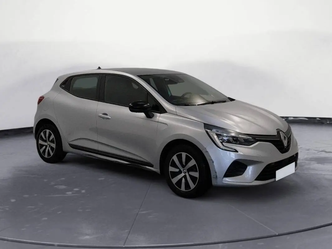 Renault Clio gris clair vue 3/4 avant droit, avec jantes noires et calandre marquée, sur fond neutre intérieur.