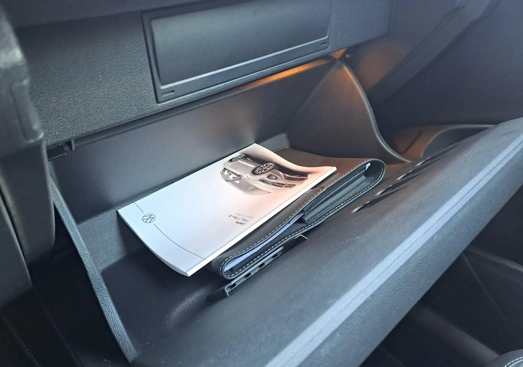 Gant de boîte à gants ouvert montrant un manuel et un porte-documents dans l'habitacle noir du Volkswagen T-Roc.