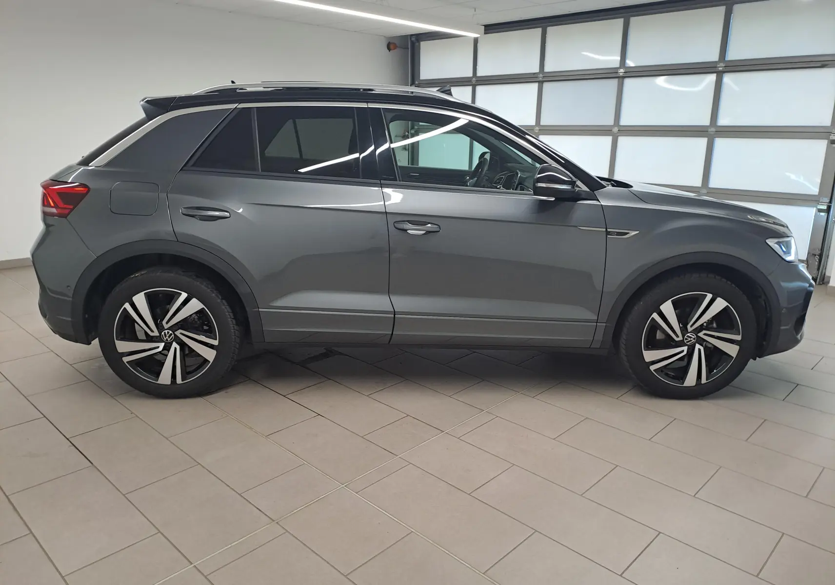 Vue de profil droit d'un Volkswagen T-Roc 2025 gris Indium avec toit noir et jantes R-Line distinctives.