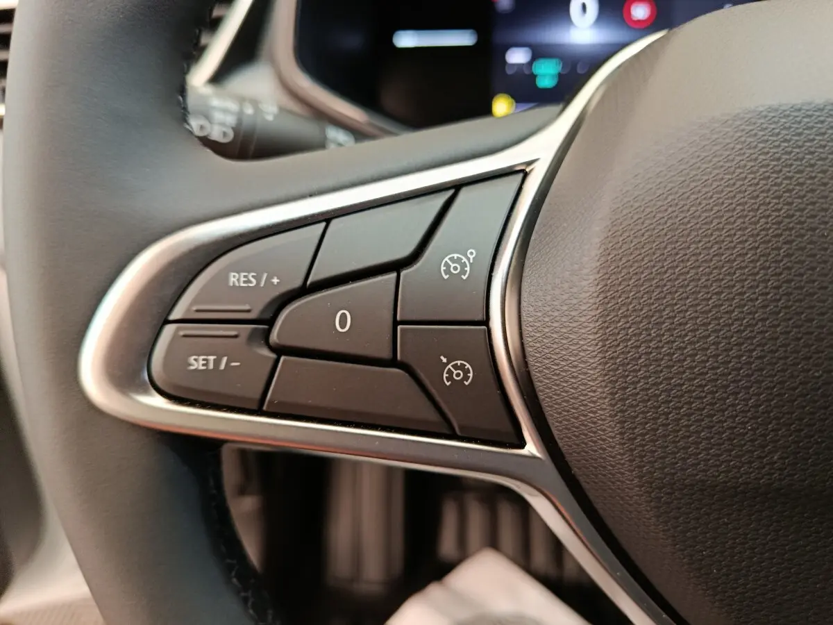 Gros plan sur les commandes du régulateur de vitesse au volant cuir de la Renault Clio blanche 2024.