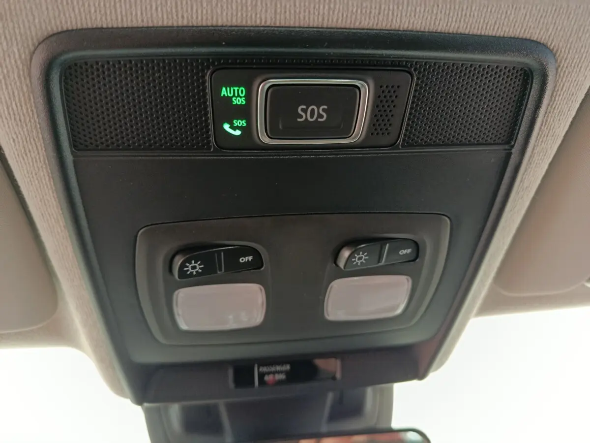 Vue en contre-plongée du panneau de commande de plafonnier noir avec bouton SOS éclairé dans une Renault Clio blanche 2024.