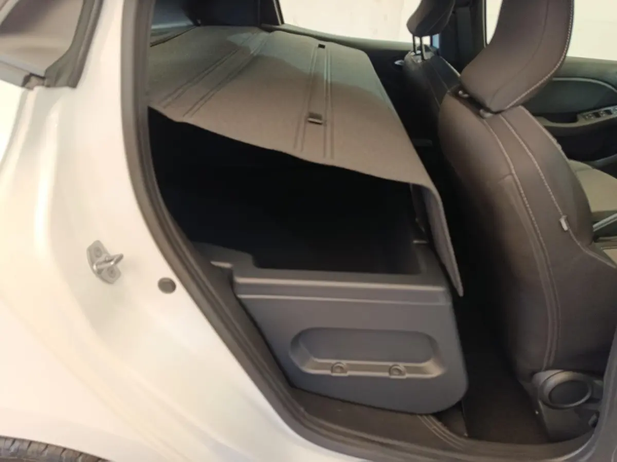 Vue intérieure côté gauche arrière d’une Renault Clio blanche 2024 montrant le coffre sous le siège arrière relevé.