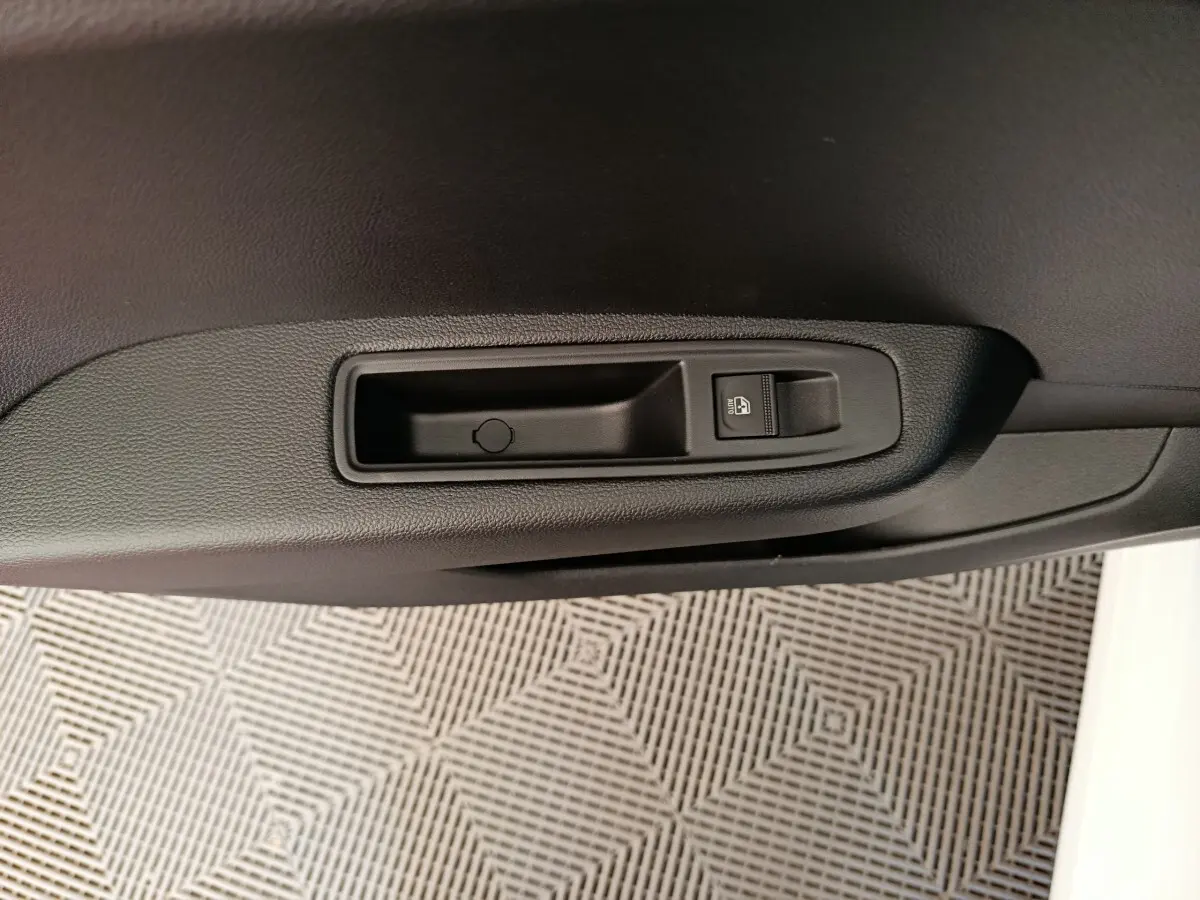 Détail de la commande de verrouillage des portes sur la portière intérieure noire d'une Renault Clio blanche.