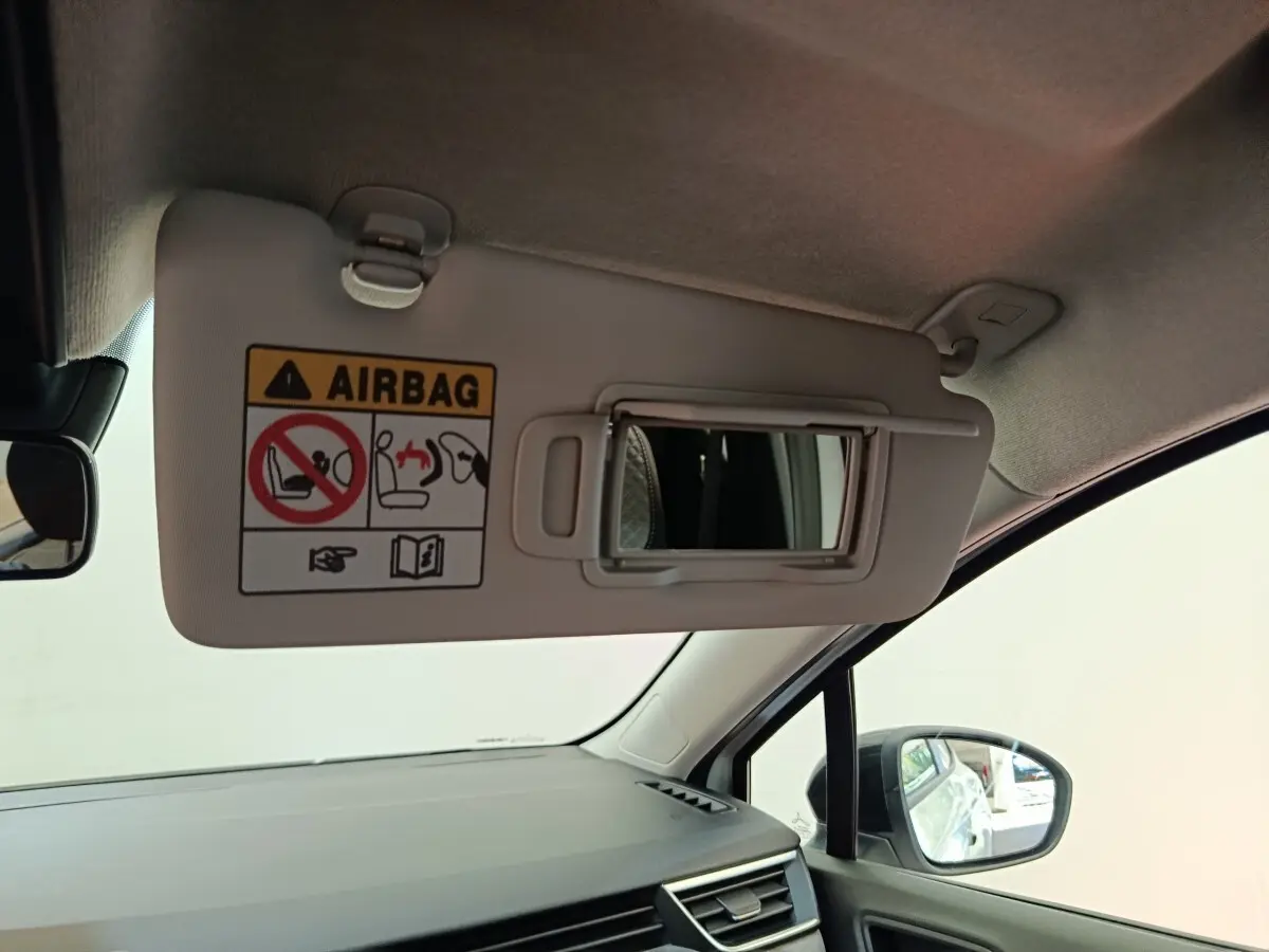 Vue intérieure côté passager de la Renault Clio blanche 2024, pare-soleil avec miroir et avertissement airbag visible.