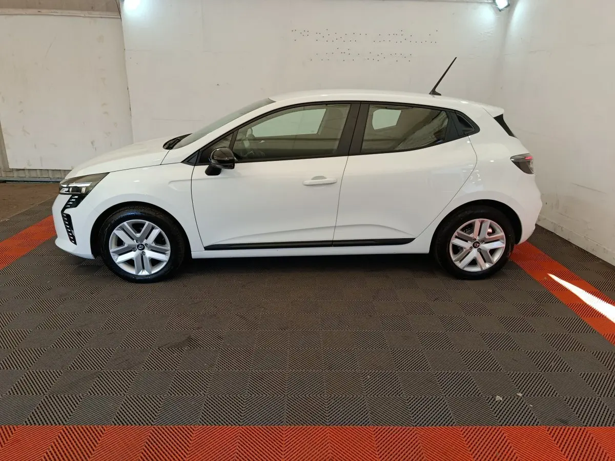 Profil droit d'une Renault Clio blanche 2024 garée en intérieur sur un sol à damiers gris et rouge.