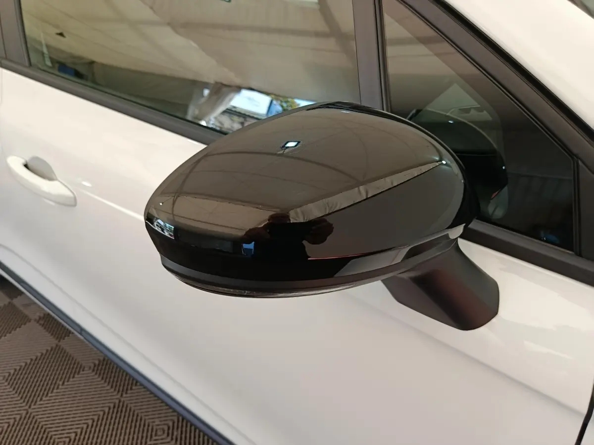 Rétroviseur noir en gros plan côté gauche d’une Renault Clio blanche 2024 avec poignée de porte visible.