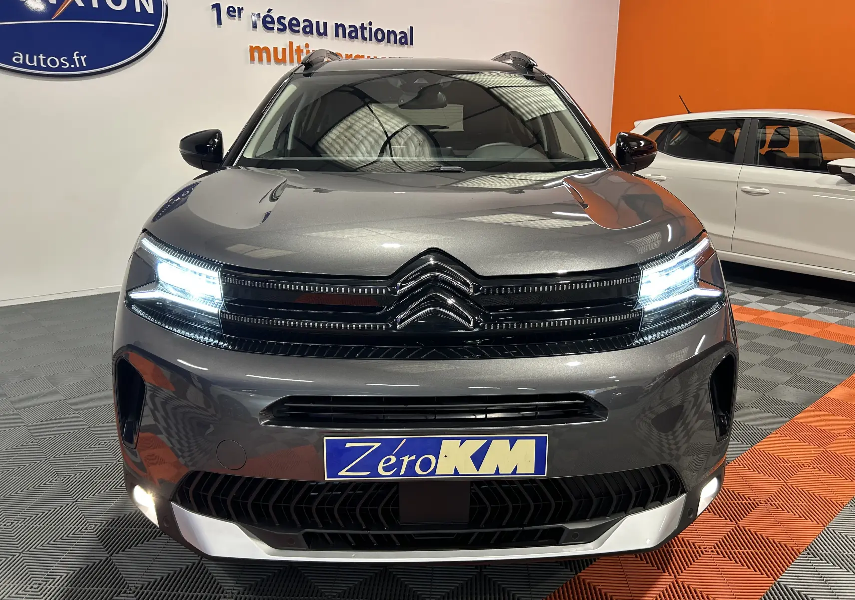 Vue avant d'un Citroën C5 Aircross gris platinium avec phares LED allumés dans un showroom.