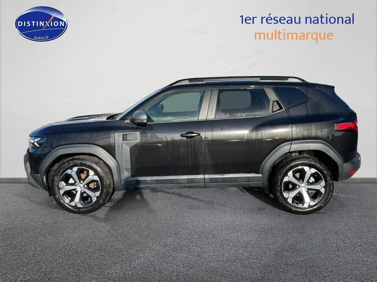 Vue de profil côté gauche d'un Dacia Duster noir 2026 avec jantes alu et barres de toit visibles.