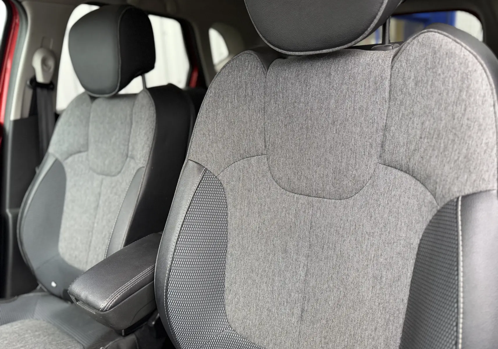 Gros plan sur les sièges avant gris et noir du Renault Captur rouge, mettant en valeur l'accoudoir central et les textures du tissu.