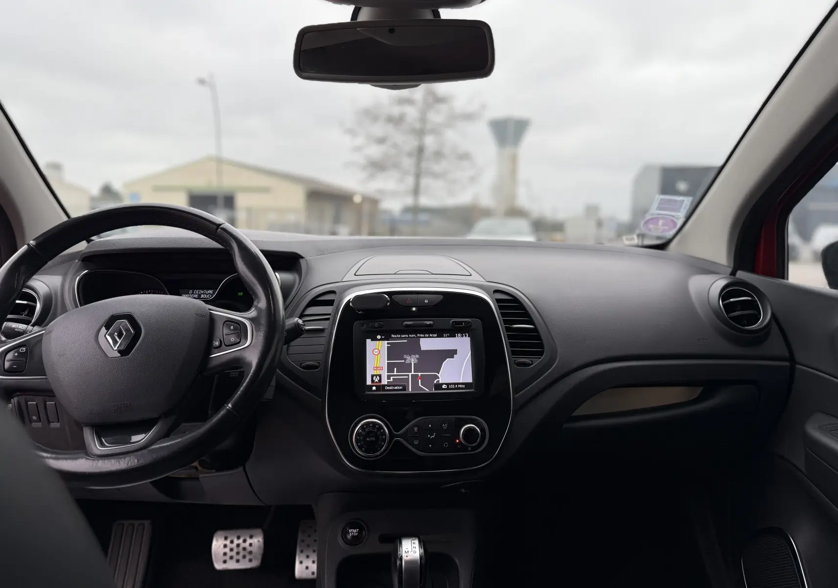 Vue intérieure frontale du tableau de bord du Renault Captur rouge 2017 avec écran tactile GPS et volant multifonction.