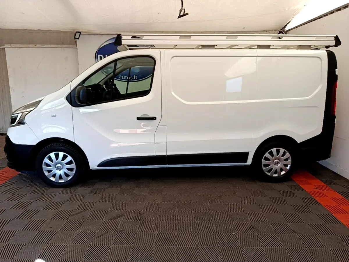 Profil latéral droit d’un Renault Trafic Fourgon blanc 2021 avec galerie de toit et jantes tôles argentées.
