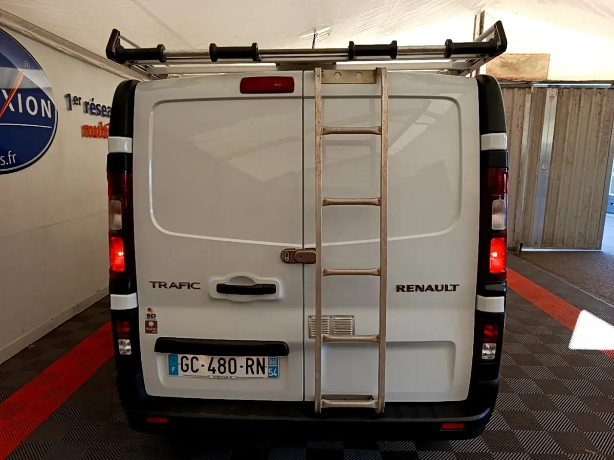 Vue arrière du Renault Trafic Fourgon blanc avec échelle métallique fixée sur la porte et feux arrière allumés.