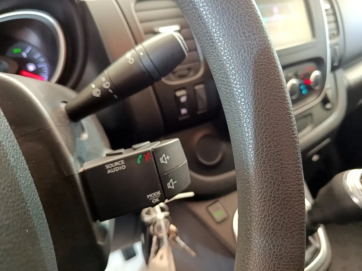 Gros plan sur le volant noir et la commande audio au volant du Renault Trafic Fourgon blanc, version 2021.