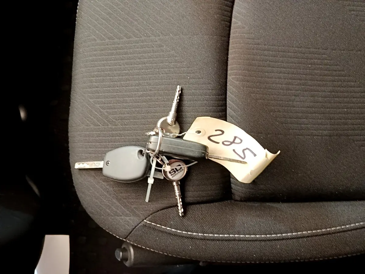 Jeu de clés avec télécommande posé sur un siège avant en tissu gris foncé à coutures blanches du Renault Trafic Fourgon blanc.