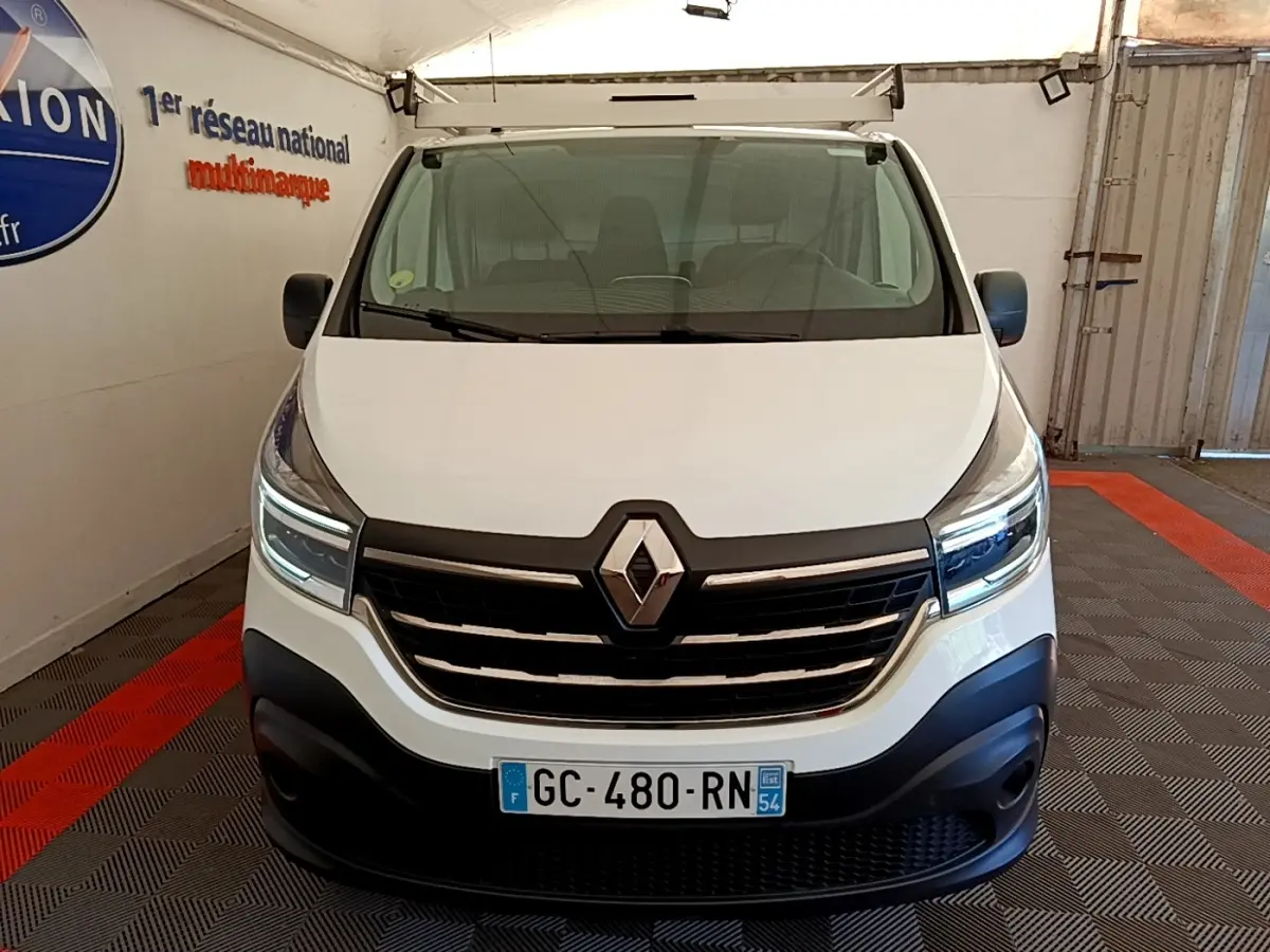 Vue frontale d’un Renault Trafic Fourgon blanc 2021 avec calandre noire et feux LED allumés dans un garage.