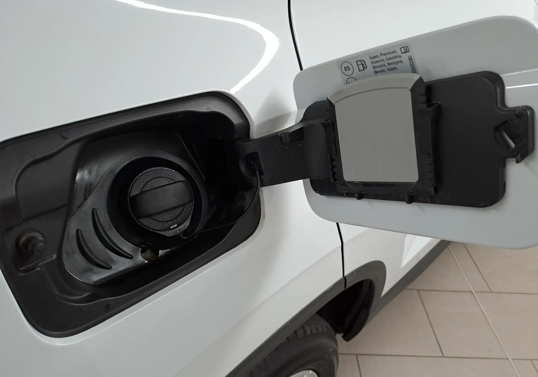 Gros plan sur la trappe à carburant ouverte côté gauche d’un Skoda Karoq blanc Lune avec bouchon essence visible.