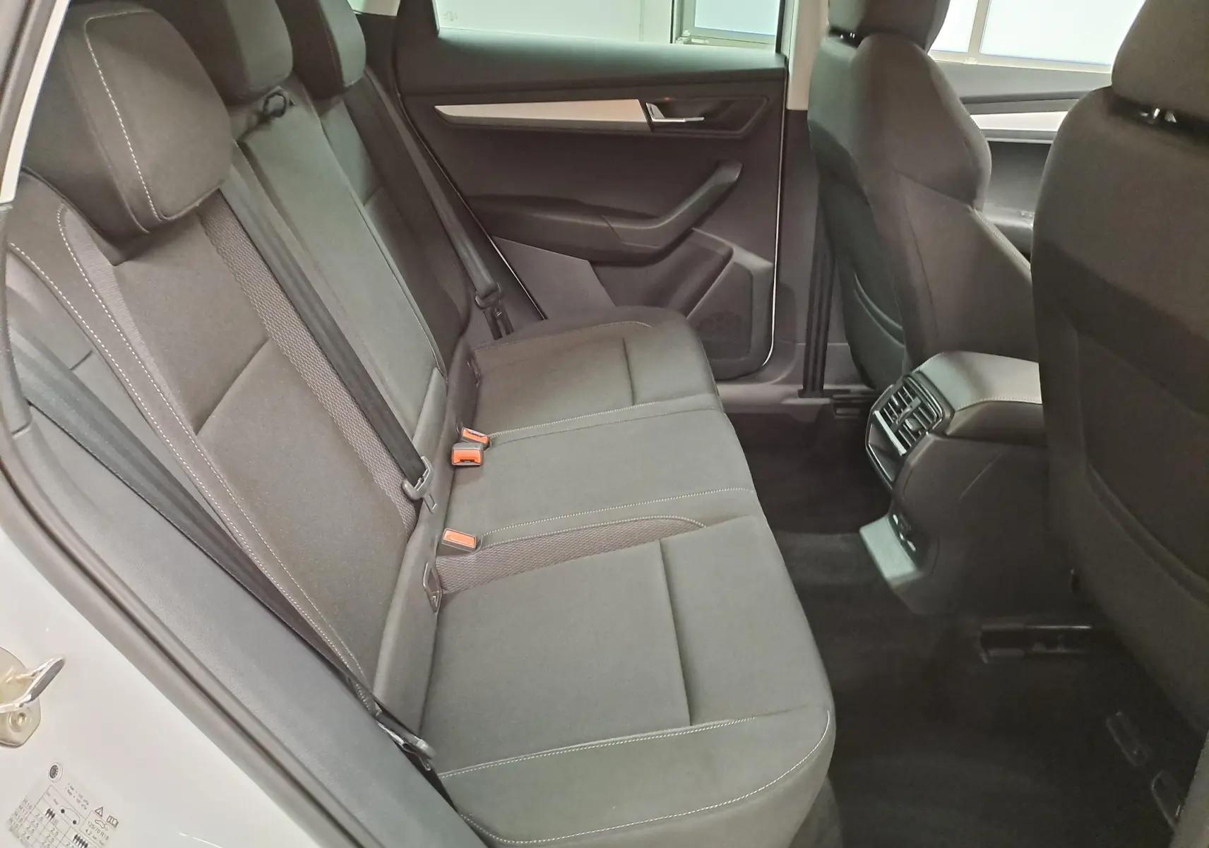 Vue intérieure arrière droite du Skoda Karoq blanc Lune 2025, sièges tissu gris avec surpiqûres contrastées.