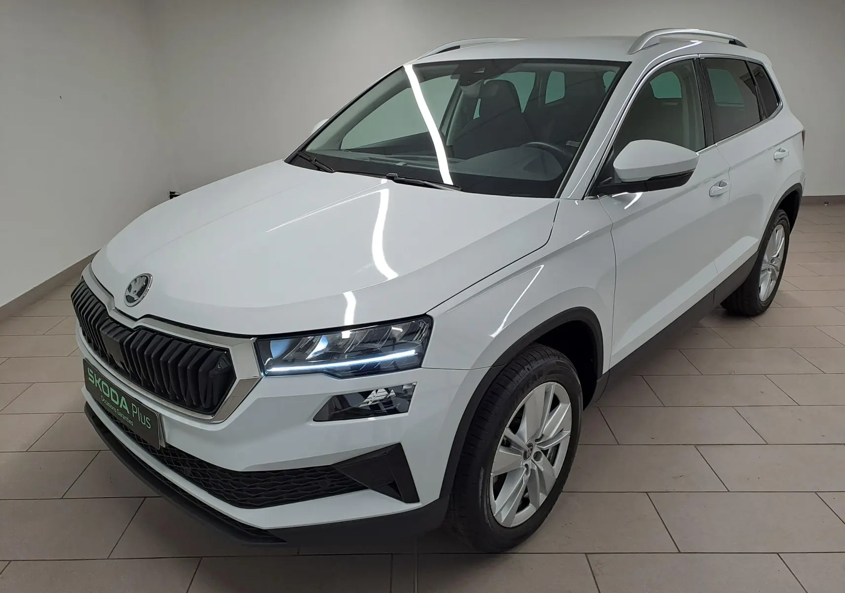Vue 3/4 avant droite du Skoda Karoq blanc Lune avec calandre noire, phares LED et rampes de pavillon argentées.