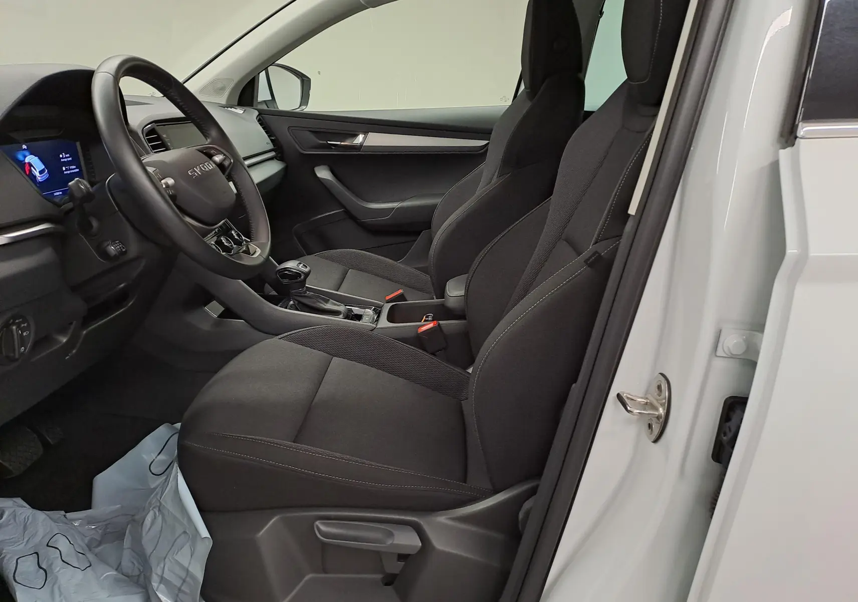 Vue intérieure côté conducteur du Skoda Karoq blanc Lune 2025, sièges noirs et tableau de bord moderne avec volant multifonction.