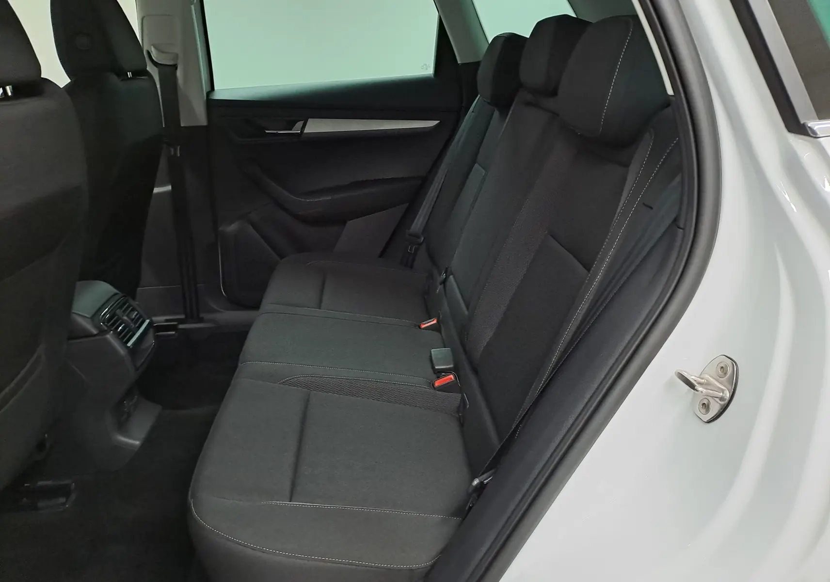 Vue intérieure côté droit des sièges arrière noirs du Skoda Karoq blanc Lune, avec porte ouverte et habillage sobre.