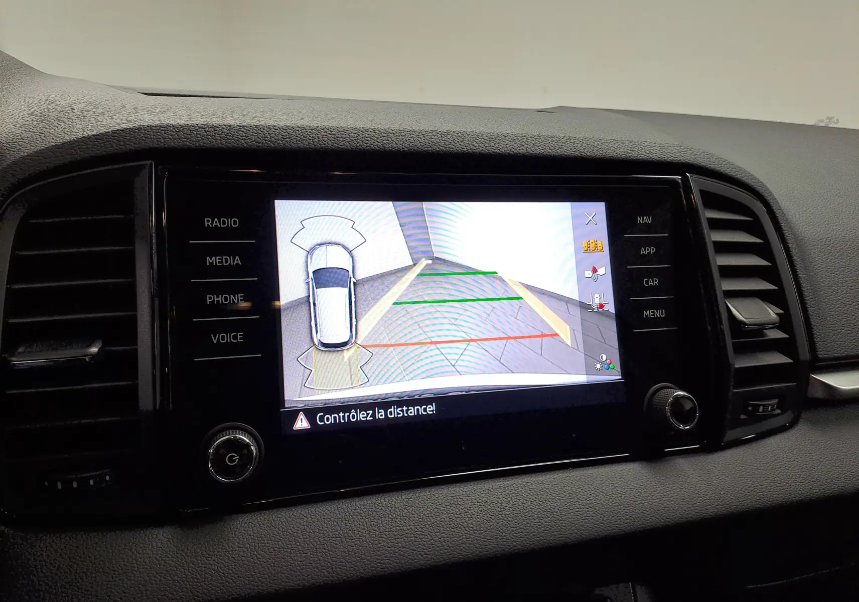 Écran central du Skoda Karoq blanc Lune 2025 affichant la caméra de recul avec repères de distance colorés.