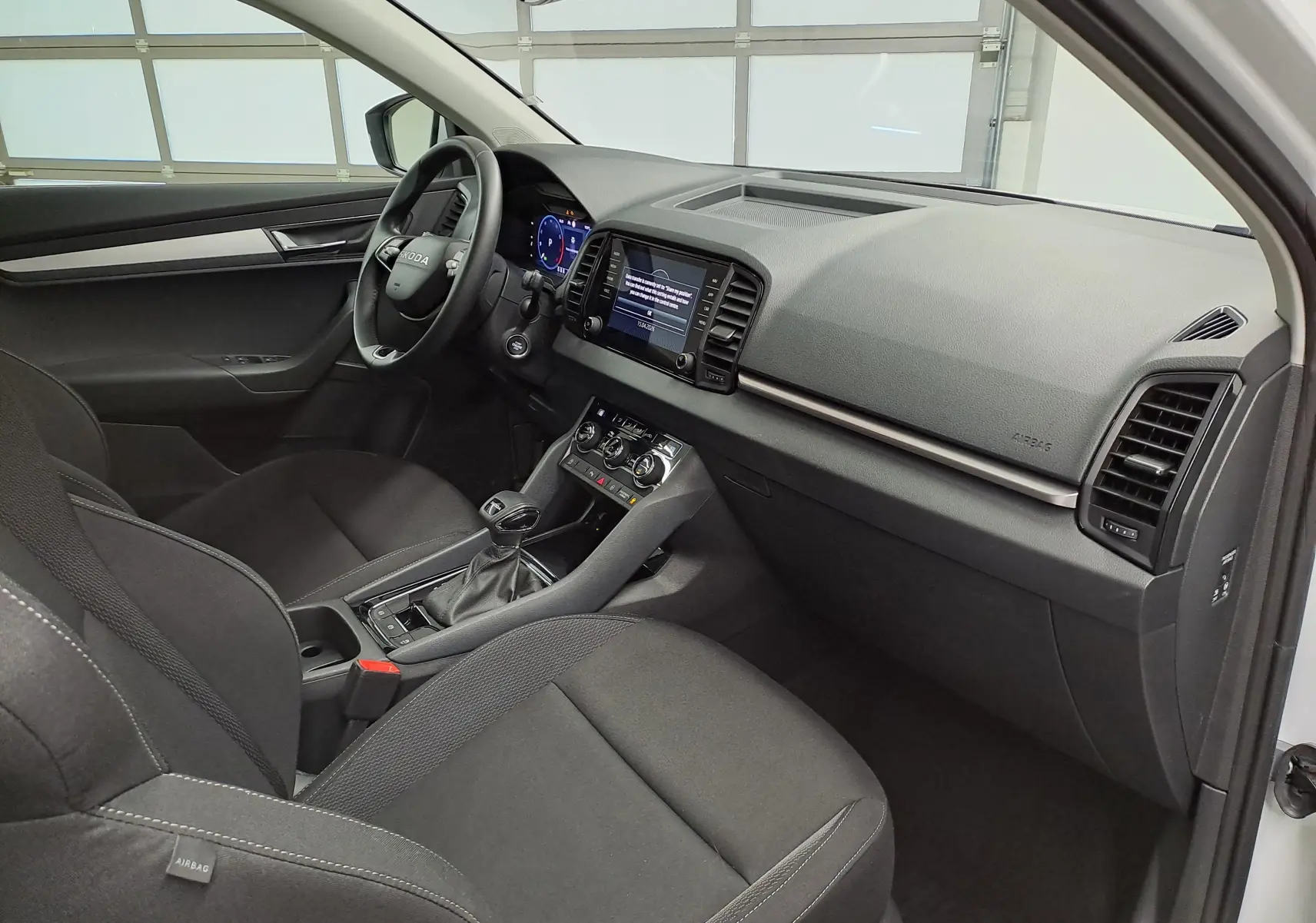 Vue intérieure côté conducteur du Skoda Karoq 2025, tableau de bord moderne avec écran tactile et sièges noirs tissu.