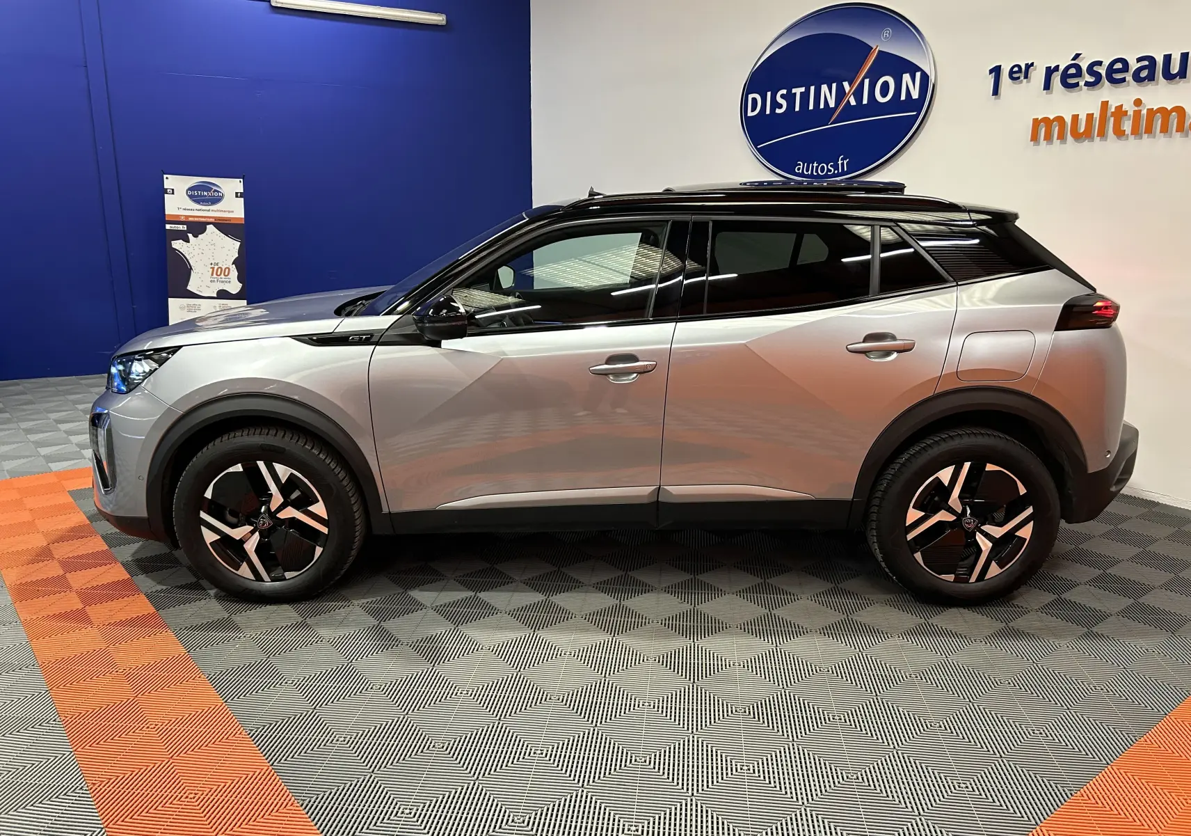 Profil droit du Peugeot 2008 BlueHDi 130 GT PACK gris Artense, avec toit noir et jantes bi-ton en intérieur showroom.