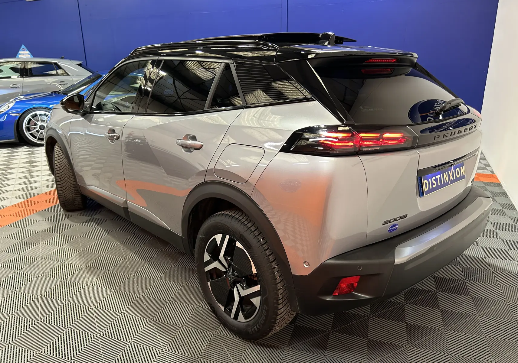 Peugeot 2008 BlueHDi 130 gris Artense en 3/4 arrière droit, toit noir et feux arrière allumés dans un showroom.