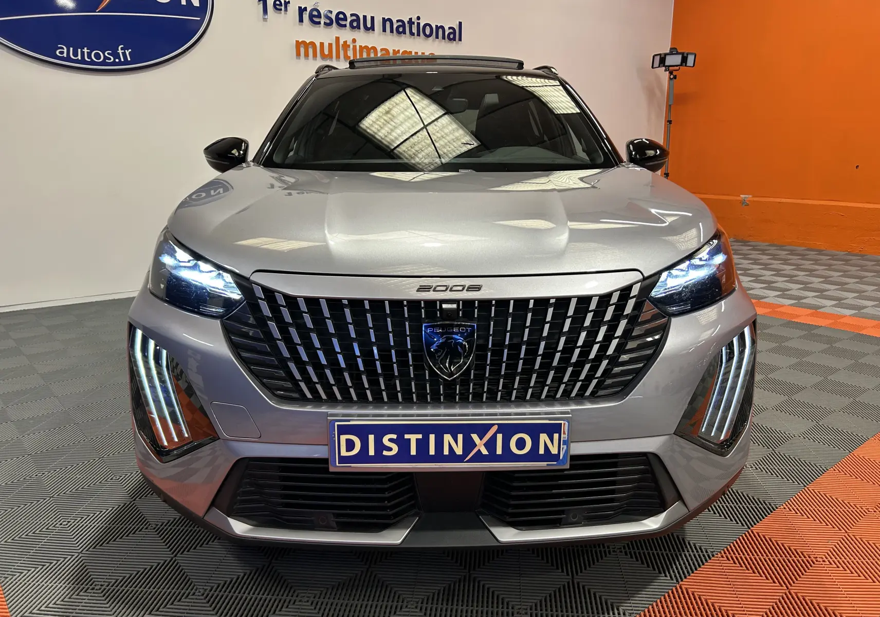 Vue avant d'un Peugeot 2008 gris Artense avec calandre noire et feux LED allumés dans un showroom.