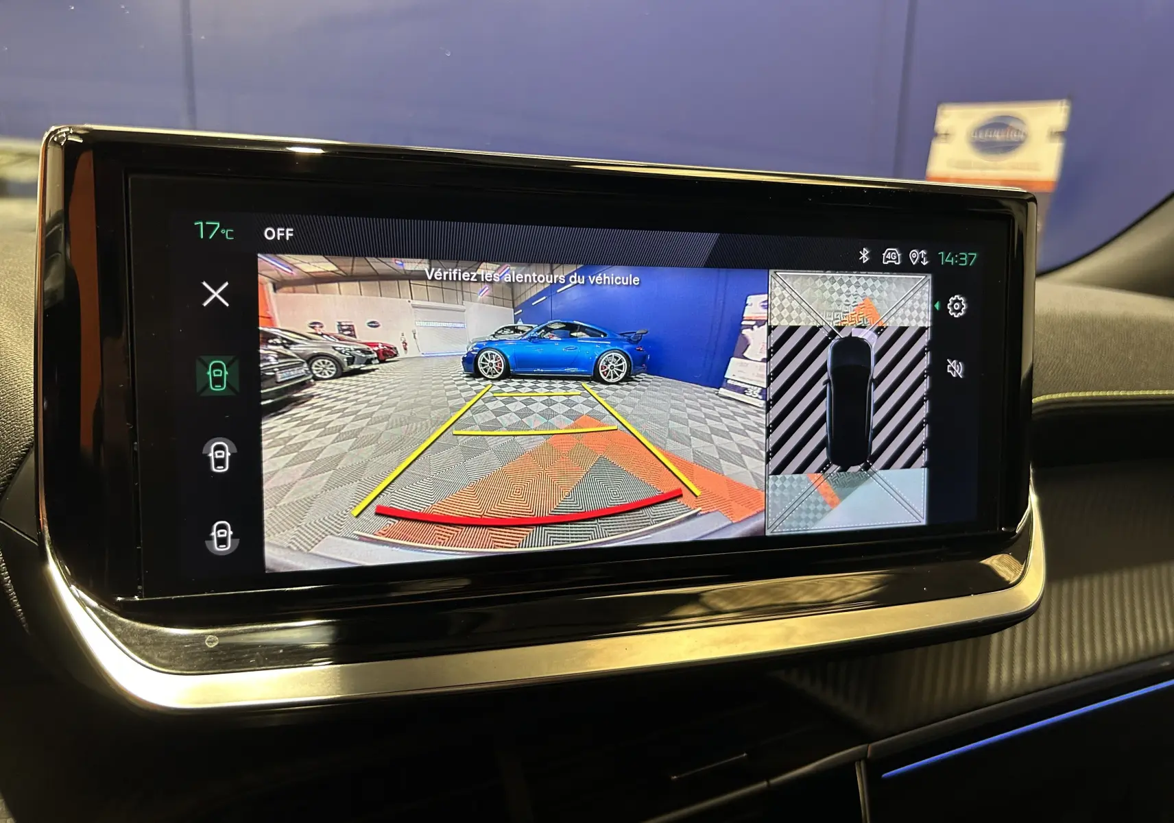 Écran multimédia montrant la caméra 360° avec vue arrière et latérale d’un véhicule bleu dans un garage.