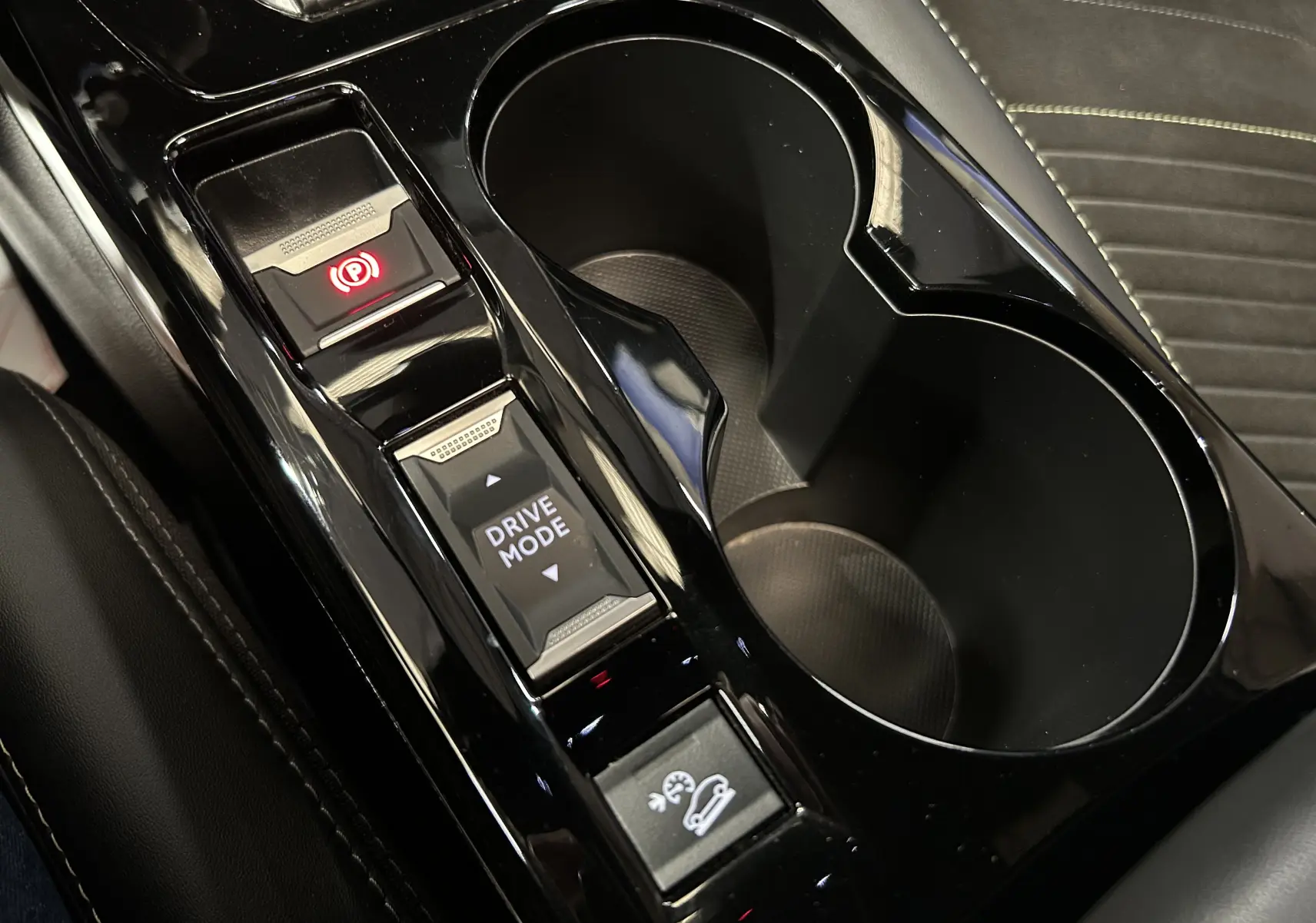 Gros plan sur la console centrale noire brillante du Peugeot 2008 2024 avec boutons frein à main, mode de conduite et assistance descente.