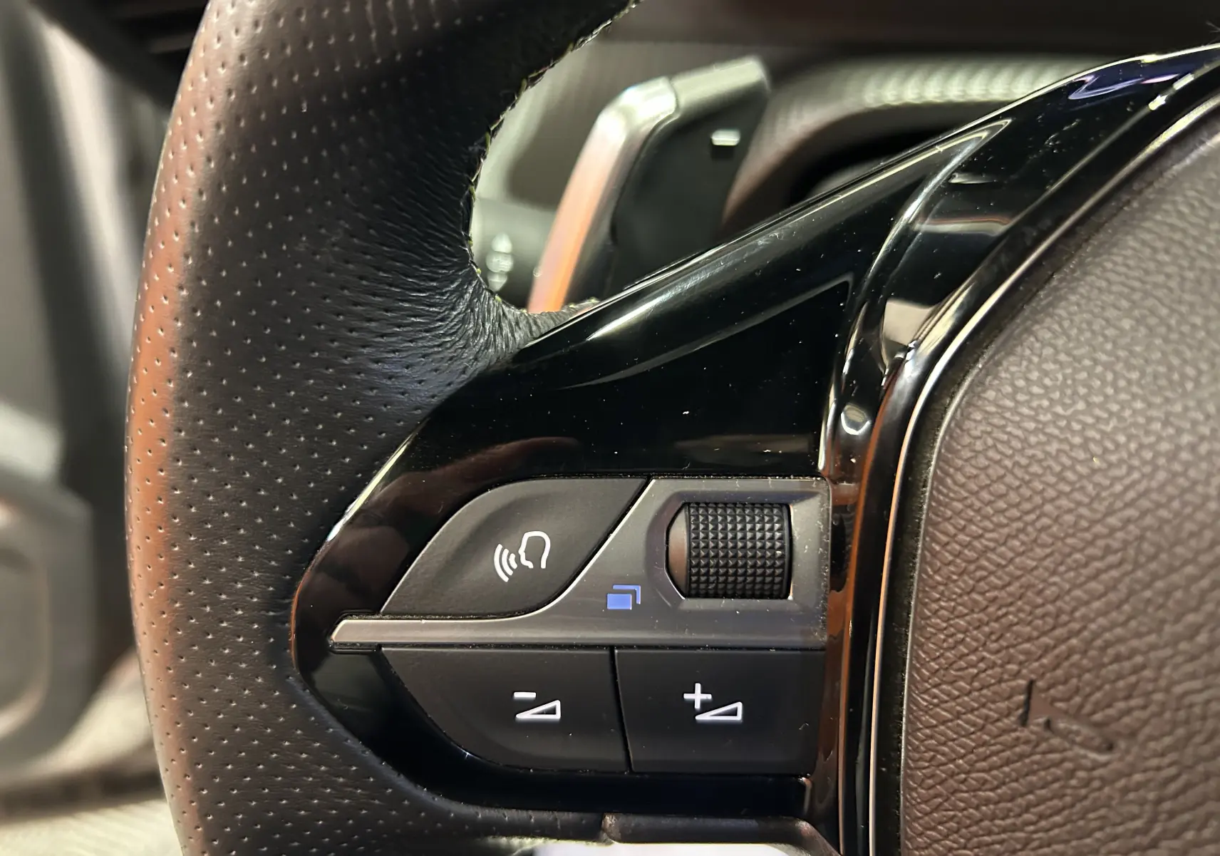 Gros plan sur les commandes du volant en cuir perforé du Peugeot 2008 gris Artense, avec molette et boutons de volume.
