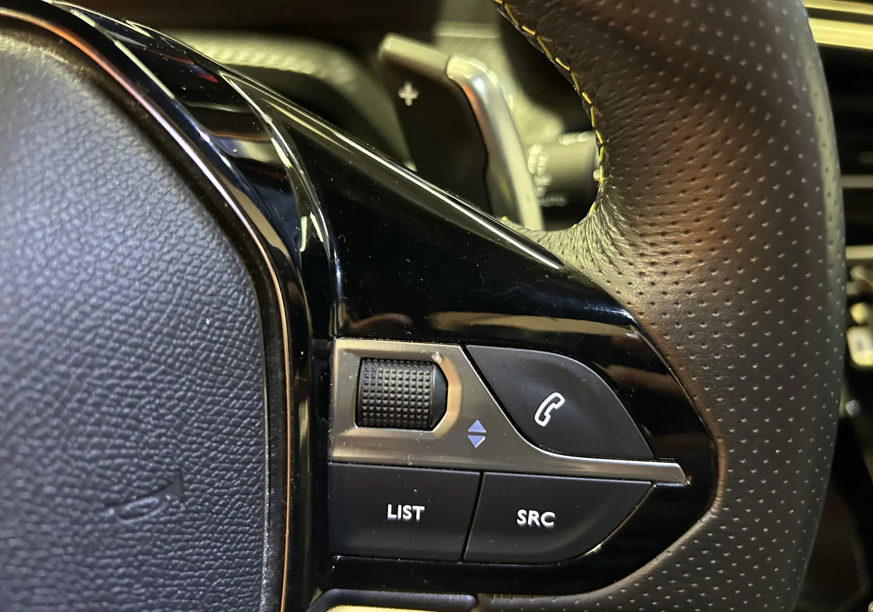 Gros plan sur les commandes gauche du volant en cuir perforé du Peugeot 2008 Gris Artense, avec molette et boutons fonction téléphone.