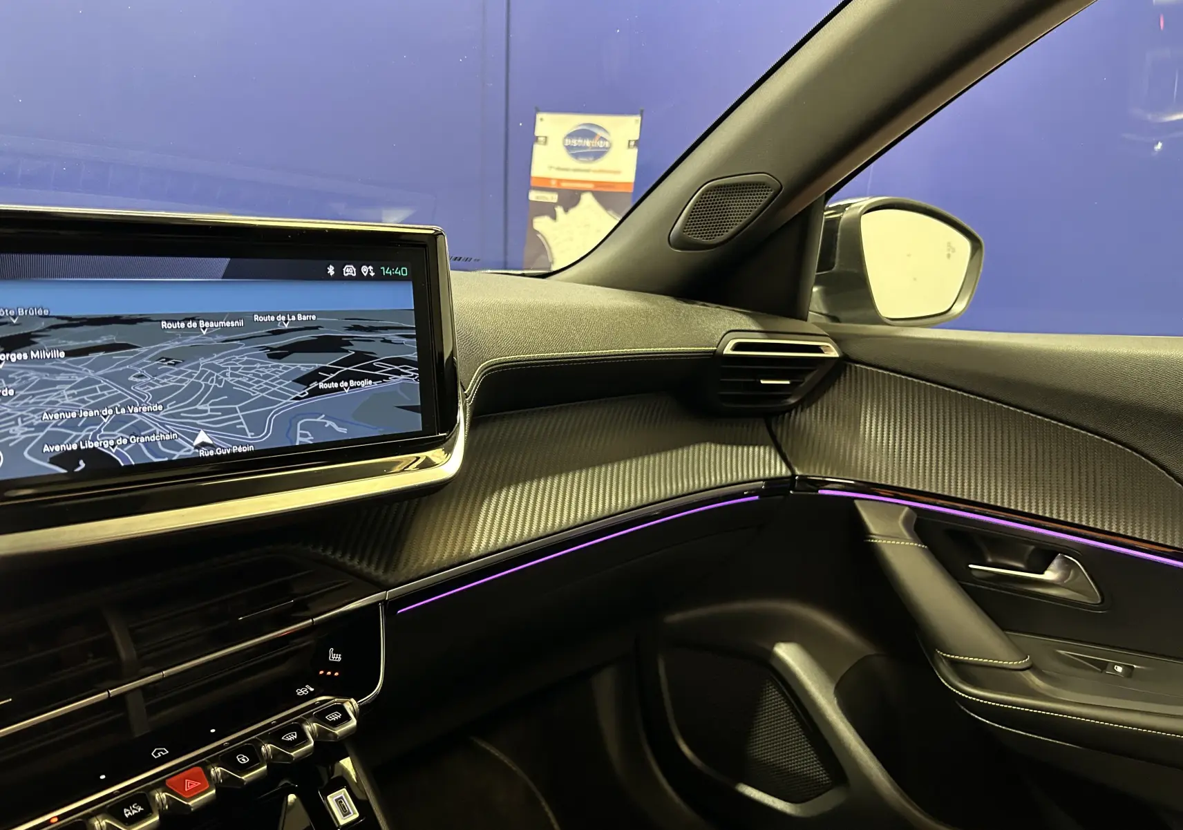 Vue intérieure côté passager du Peugeot 2008 GT Pack 2024 avec écran GPS, éclairage d’ambiance violet et finitions carbone.