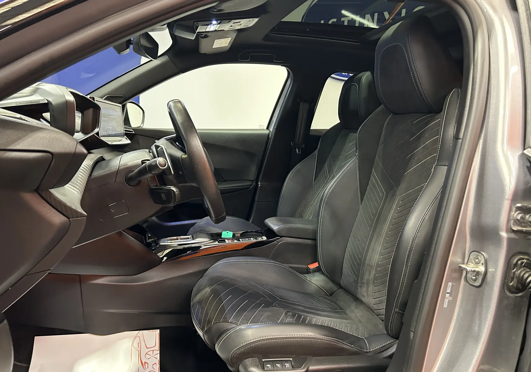 Vue intérieure côté conducteur du Peugeot 2008 gris Artense 2024, sièges cuir Alcantara avec surpiqûres et toit panoramique.