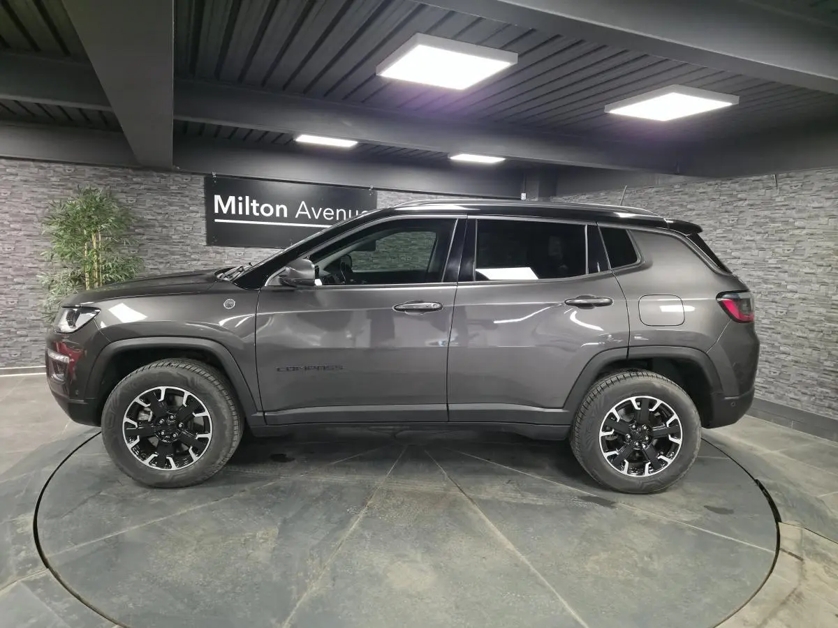 Vue de profil côté gauche d’un Jeep Compass gris métallisé avec toit noir et jantes noires en showroom.