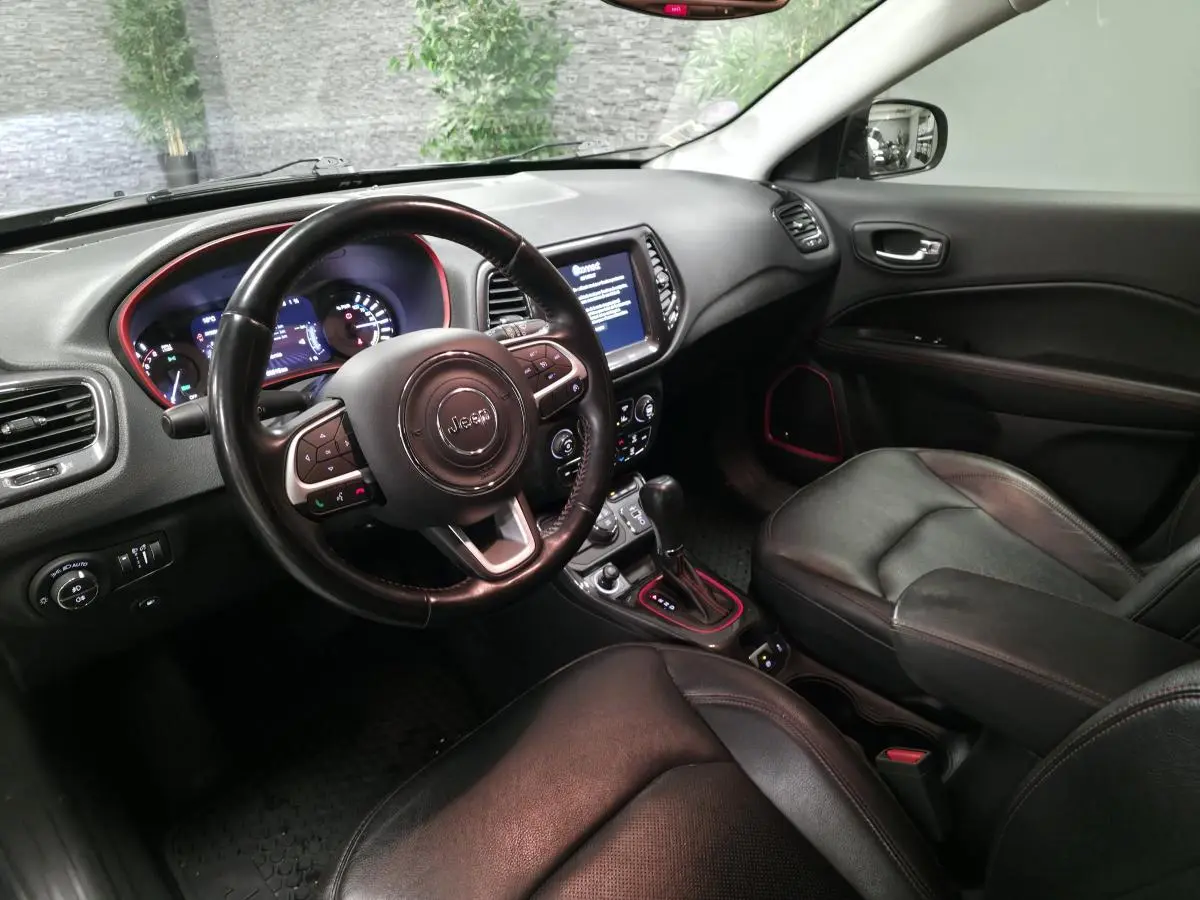 Vue intérieure côté conducteur de la Jeep Compass Trailhawk 2020, sellerie cuir noire avec surpiqûres rouges et tableau de bord moderne.