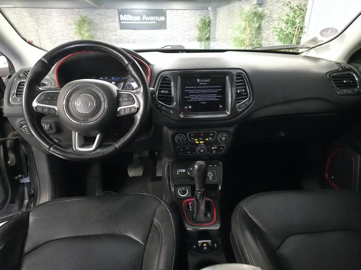 Vue intérieure du tableau de bord et volant noir du Jeep Compass Trailhawk 2020 avec écran tactile central et détails rouges.