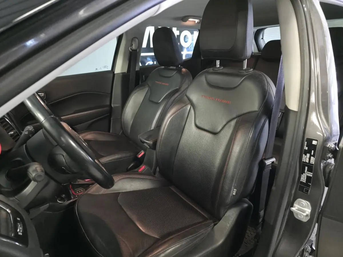 Vue intérieure côté conducteur du Jeep Compass gris, sièges cuir noirs avec logo Trailhawk brodé en rouge.
