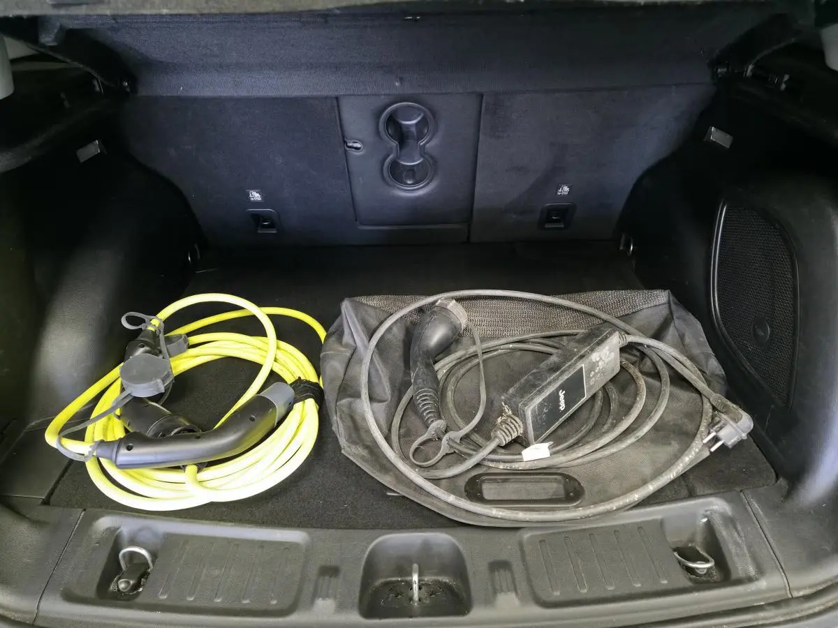 Coffre ouvert d’un Jeep Compass gris montrant deux câbles de recharge pour véhicule hybride rechargeable.