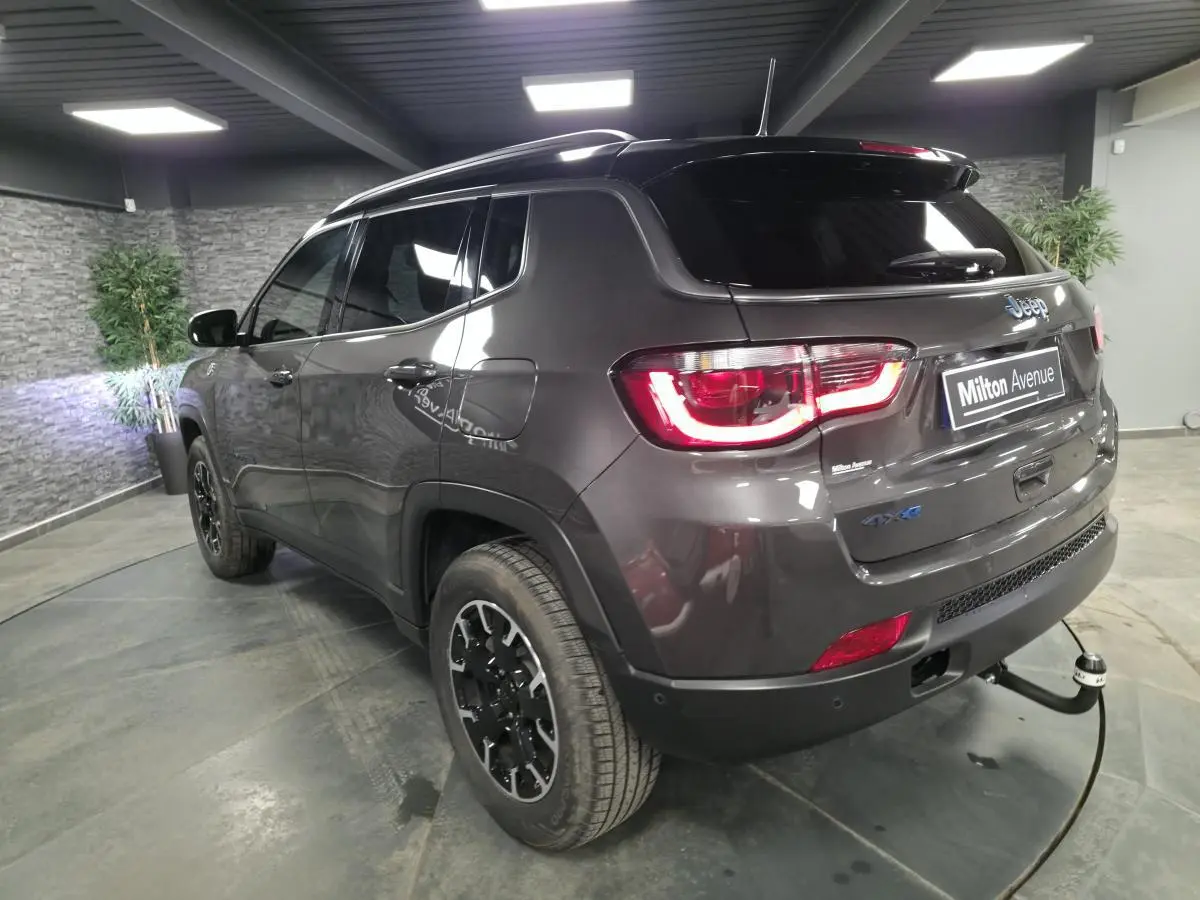 Vue 3/4 arrière droite du Jeep Compass gris métallisé avec attelage fixe et toit noir dans un showroom.