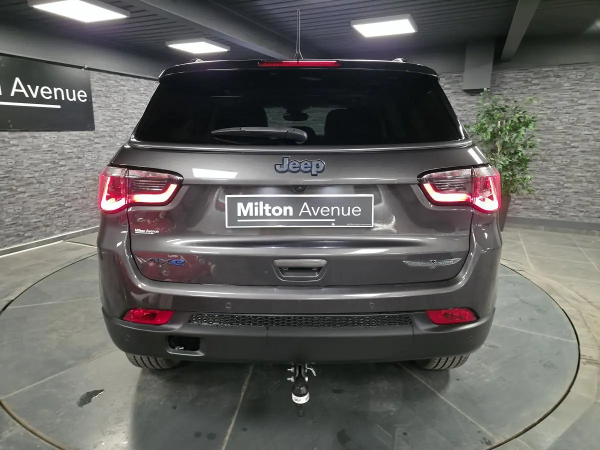 Vue arrière d'un Jeep Compass gris métallisé avec hayon électrique et attelage fixe visible en intérieur.