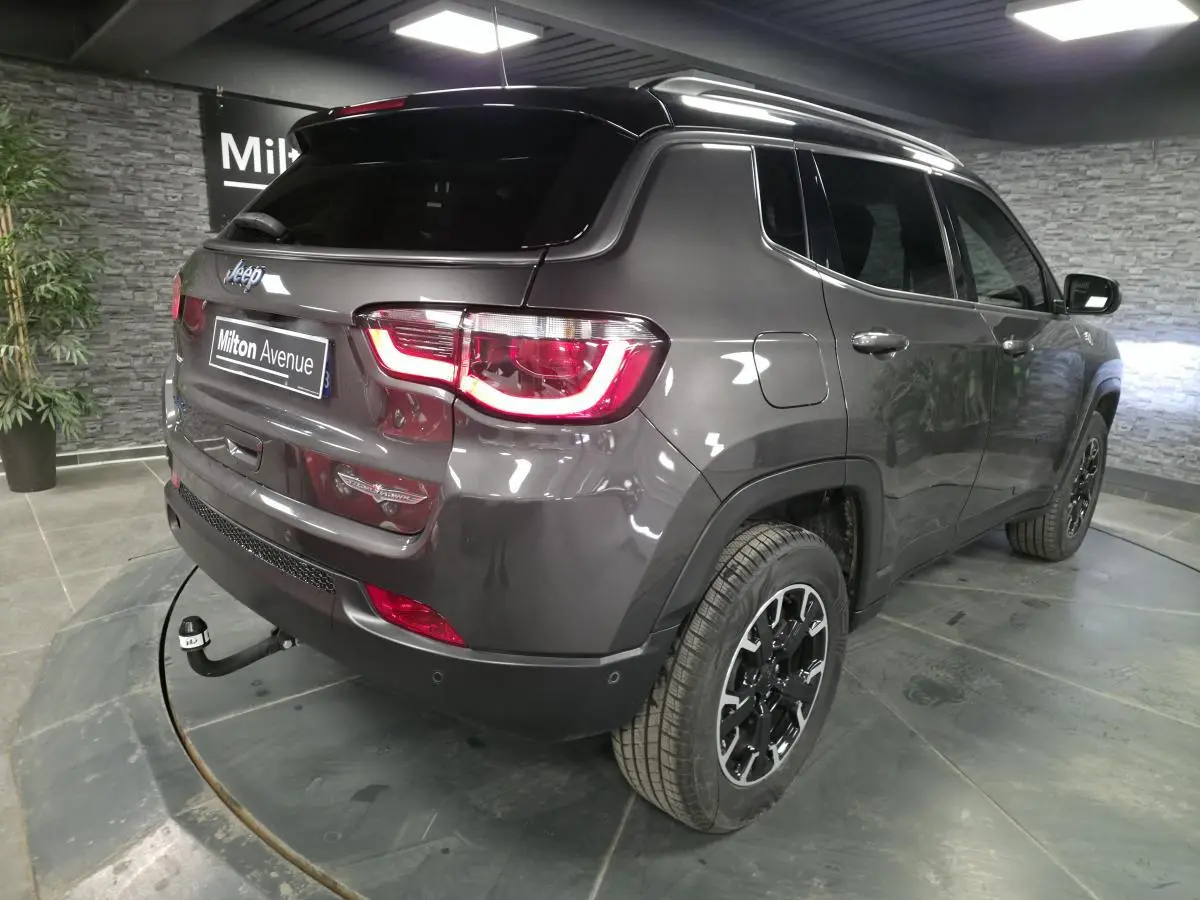 Jeep Compass gris métallisé en 3/4 arrière droit avec attelage fixe et toit noir dans un showroom.